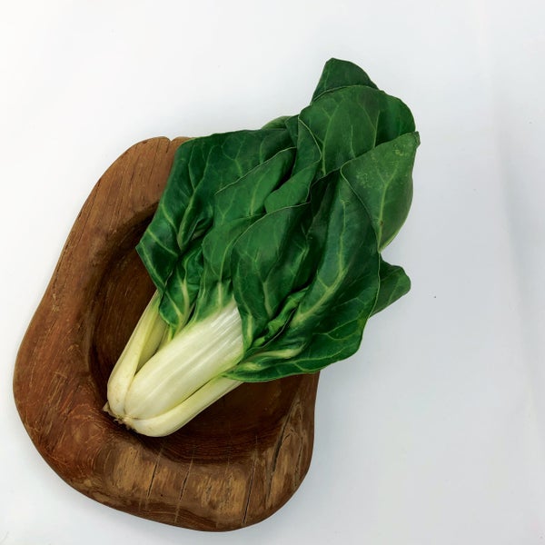 Frischer Mangold mit großen grünen Blättern und weißen Stielen in einer rustikalen Holzschale.