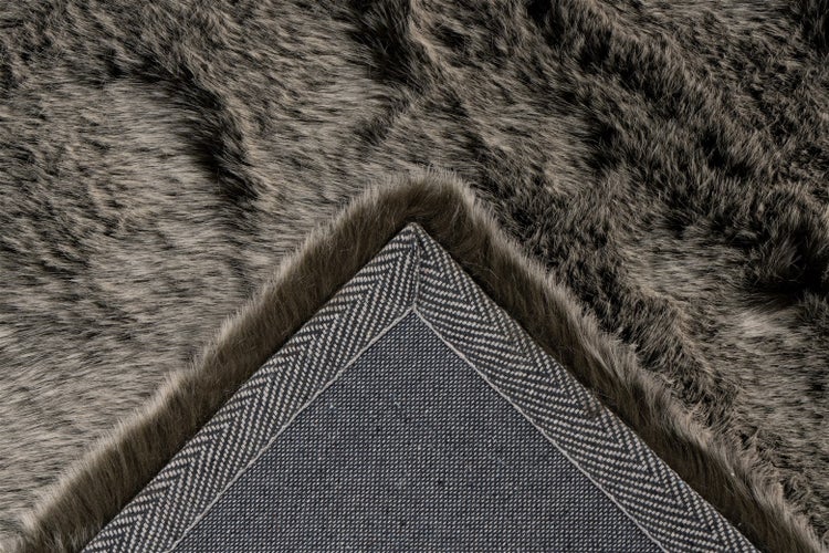 Nahaufnahme eines Kunstfellteppichs mit weichem Flor und rutschfester Rückseite mit Fischgrätenmuster.