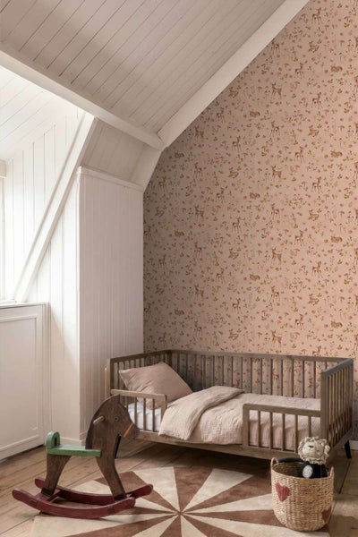 Kinderzimmer mit Tapete mit Rehmotiv, Holzgitterbett und Schaukelpferd auf Holzboden in einem Dachgeschosszimmer.