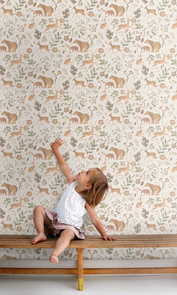 Mädchen vor einer Tapete mit Bären, Hirschen und floralen Motiven auf einer Holzbank sitzend