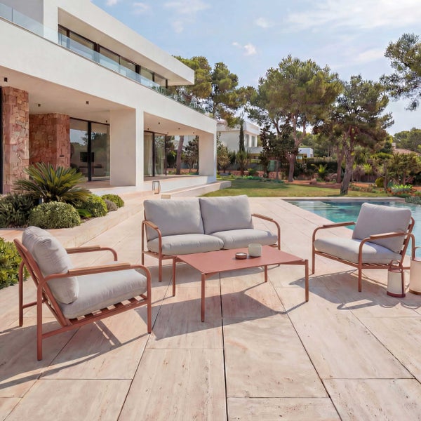 Modernes Garten-Lounge-Set aus Metall mit Zweisitzer-Sofa, zwei Sesseln und Couchtisch auf einer hellen Steinterrasse an einem Pool.