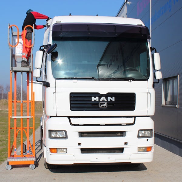 Person auf einer mobilen Arbeitsbühne bei Wartungsarbeiten an einem weißen Lastwagen.