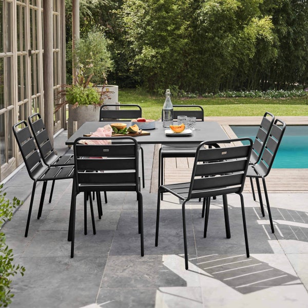 Moderne Garten-Essgruppe mit rechteckigem Metalltisch und passenden Stühlen auf einer Steinterrasse, im Hintergrund Garten, Rasen und Pool.