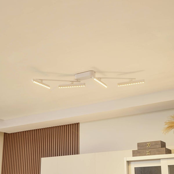 Weiße LED Deckenleuchte mit vier verstellbaren länglichen Lichtarmen in einem hellen Raum mit einer Wand aus Holzlamellen.