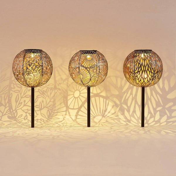 Drei Solar-Gartenleuchten mit dekorativen Metallkugeln in verschiedenen Mustern auf schwarzen Erdspießen mit warmweißem Licht.