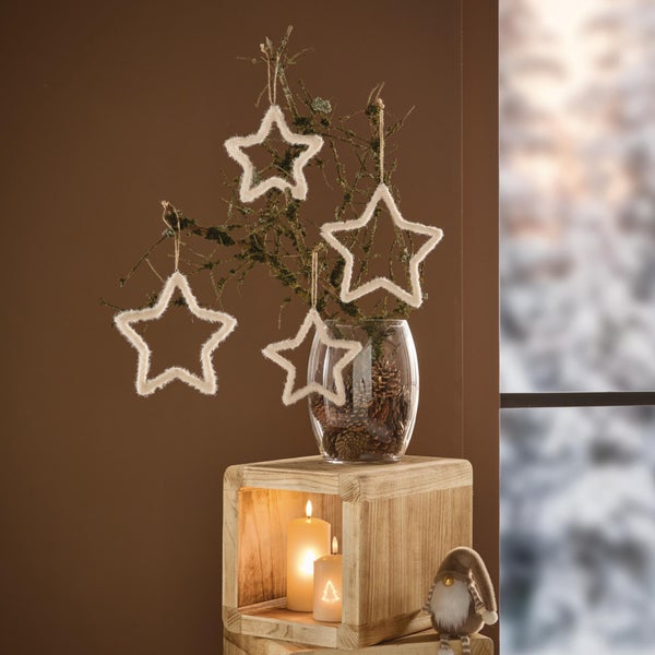 Weihnachtliche Dekoration mit hängenden Sternen an Zweigen in einer Glasvase, auf einem Holzwürfel mit Kerzen und einer Wichtelfigur platziert.