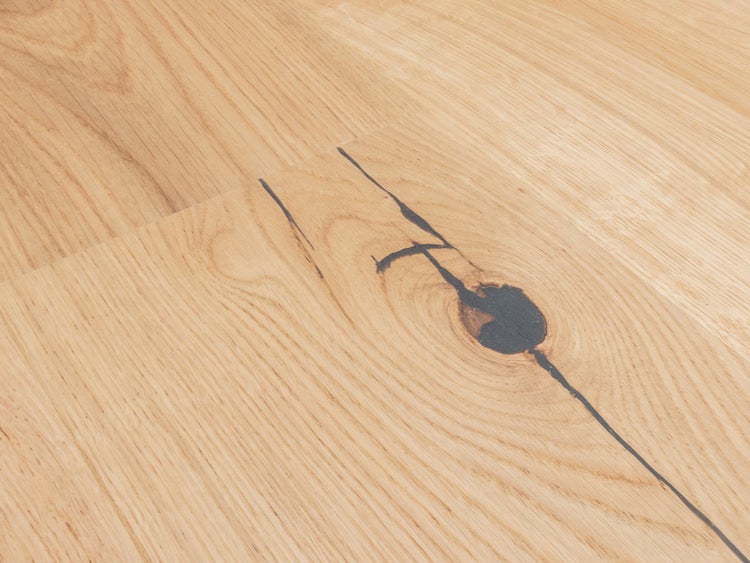 Nahaufnahme eines Holzfußbodens mit sichtbarer Maserung und einem markanten dunklen Astloch.