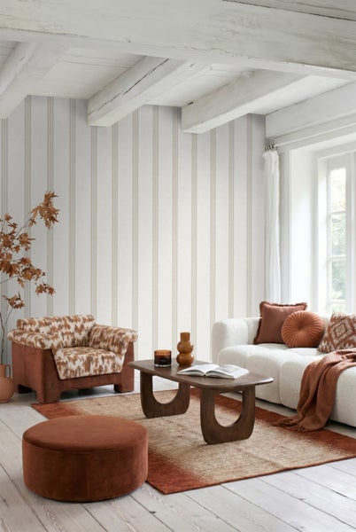 Helles Wohnzimmer mit gestreifter Tapete, strukturiertem Sofa, modernem Couchtisch aus Holz, Sessel und dekorativem Teppich in warmer Wohnatmosphäre.