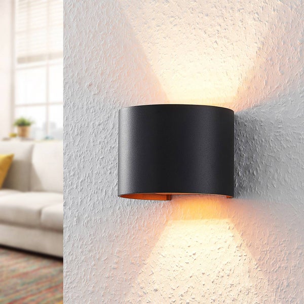 Moderne schwarze Wandleuchte aus Metall mit Up-and-Down-Lichteffekt an einer strukturierten Wand in einem hellen Wohnzimmer.