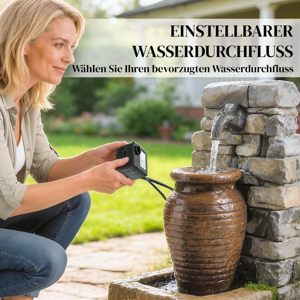 Frau stellt eine kleine schwarze Wasserpumpe mit einstellbarem Durchfluss an einem Gartenbrunnen aus Stein mit Terrakottagefäß ein.