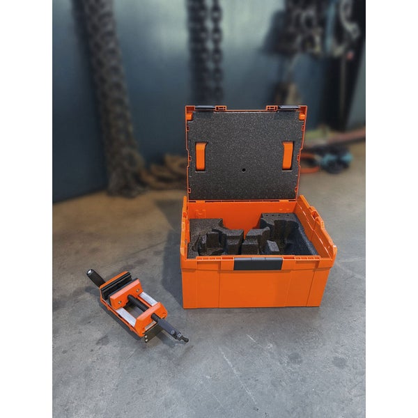 Offener orangefarbener Werkzeugkoffer mit Schaumstoffeinlage und ein Schraubstock auf einem Werkstattboden.