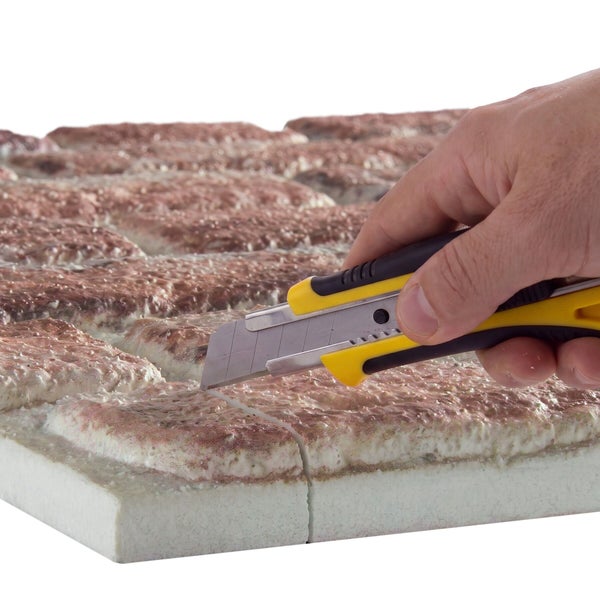 Hand schneidet mit einem Cuttermesser ein Dämmplattenelement mit Backsteinoptik zu.