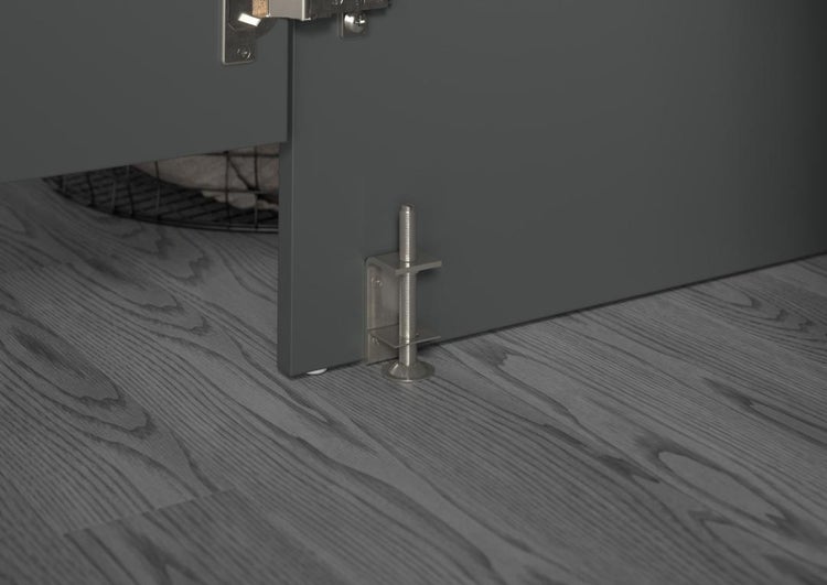 Höhenverstellbarer Sockelfuß aus Metall für Möbel, montiert an einer grauen Schrankwand auf einem Boden mit Holzoptik.