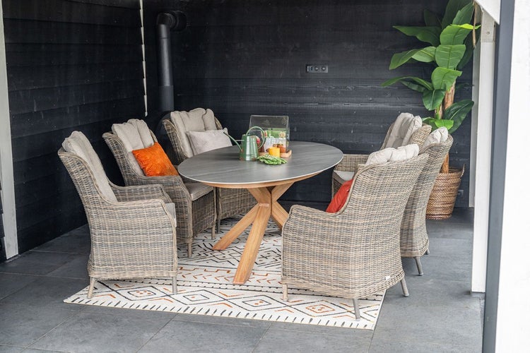 Garten-Essgruppe mit ovalem Tisch und vier Polyrattan-Geflechtsesseln auf einer Terrasse vor einer schwarzen Holzwand.