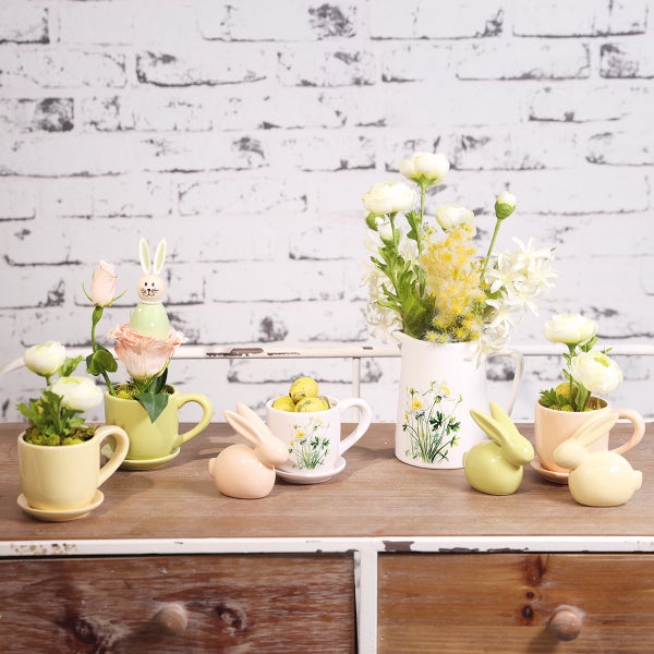 Dekoratives Osterarrangement mit Vasen, Kunstblumen und Osterhasenfiguren auf einem Tisch.