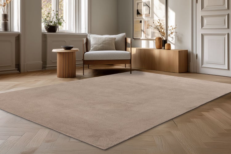 Ein unifarbener Teppich in einem modern eingerichteten Wohnraum mit Parkettboden, Sessel, Beistelltisch und Sideboard aus Holz.