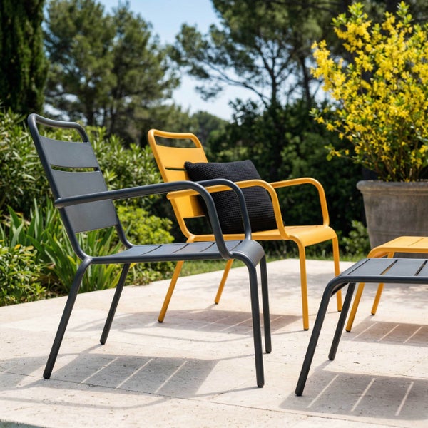 Moderne Garten-Loungesessel mit Armlehnen und passenden Fußhockern aus Metall auf einer hellen Terrasse mit Bepflanzung.