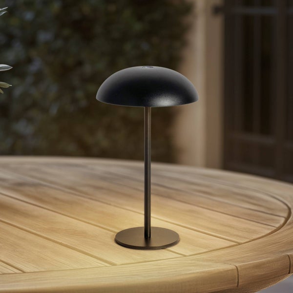 Moderne schwarze Tischleuchte mit halbkugelförmigem Schirm auf einem Holztisch, die warmes Licht abgibt.