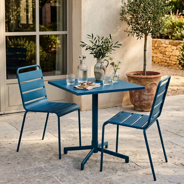 Modernes Bistro-Set aus blauem Metall auf einer Terrasse, bestehend aus einem quadratischen Tisch und zwei passenden Stühlen.