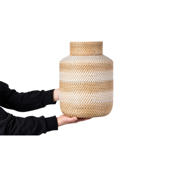 Hände halten eine zylindrische Vase aus geflochtenem Rattan in Naturoptik.