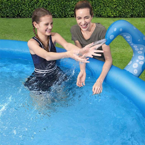 Ein Kind und eine Frau spielen in einem aufblasbaren Pool mit einem Wassersprüher in Form eines Oktopus-Tentakels im hellen Garten.