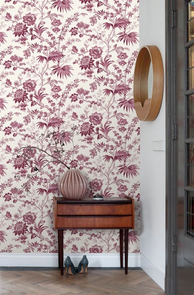 Vliestapete mit floralem Vintage-Muster in Dunkelrot in einem hellen Raum mit Holzmöbeln, Vase und rundem Spiegel.