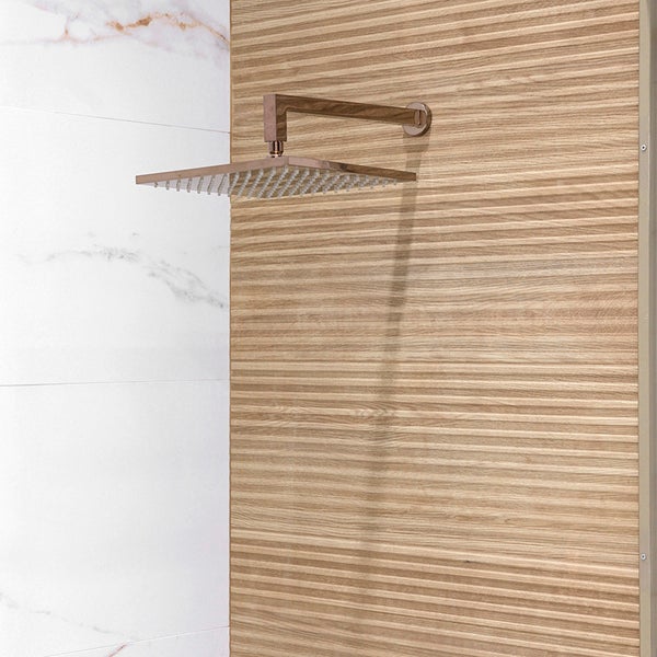 Quadratische Kopfbrause mit Wandarm installiert an einer Wand mit strukturierten Holzoptikfliesen und weißen Marmoroptikfliesen in der Dusche.