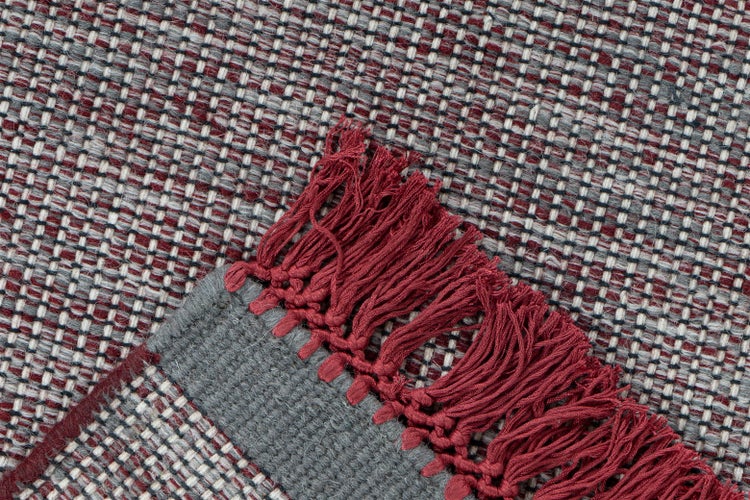 Detailansicht eines gewebten Teppichs mit Fransen und Karomuster in Rot und Grau.