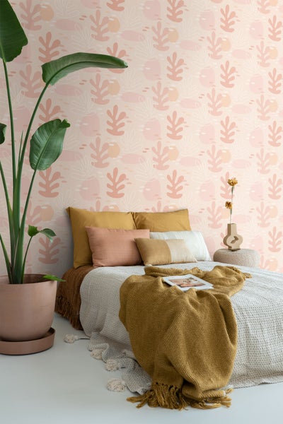 Schlafzimmer mit Bett, Kissen, Decke und Zimmerpflanze vor einer gemusterten Tapete