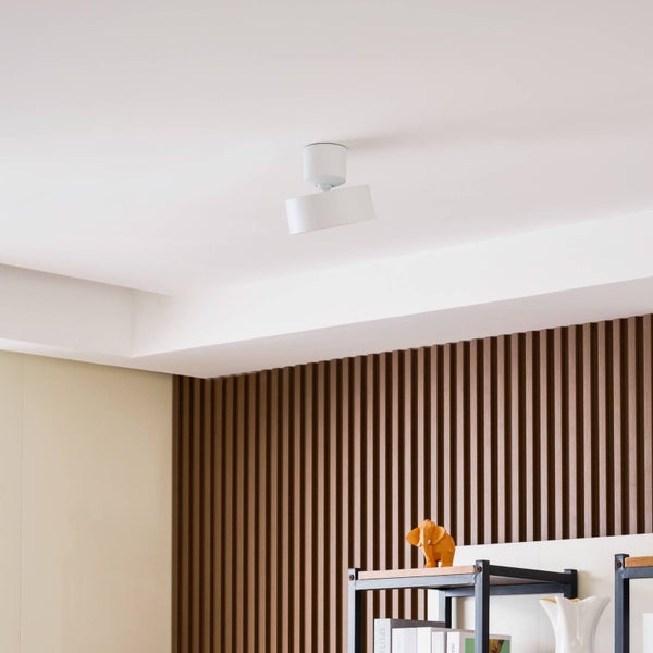 Moderne weiße Deckenleuchte an einer Decke in einem hellen Raum mit Holzlamellenwand und Regal.