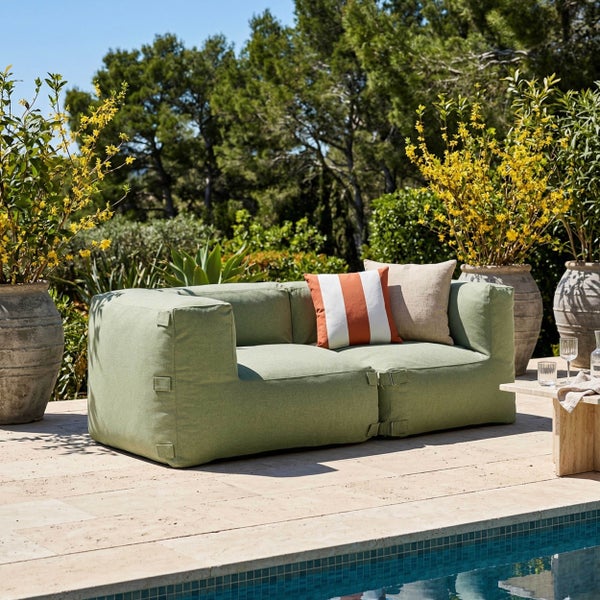Modulares Outdoor-Sofa aus zwei hellgrünen Polsterelementen auf einer Terrasse mit Dekokissen und Gartenpflanzen.