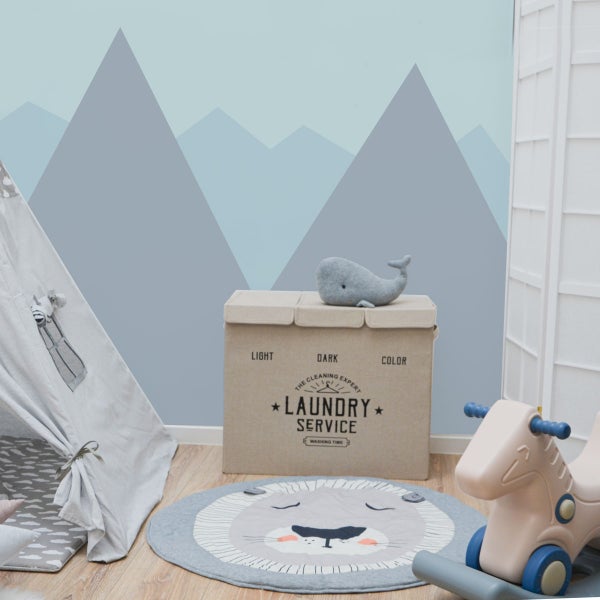 Helles Kinderzimmer mit Berg-Wandbild, Wäschekorb, Spielzelt, Löwen-Teppich und Schaukelspielzeug auf Holzboden.