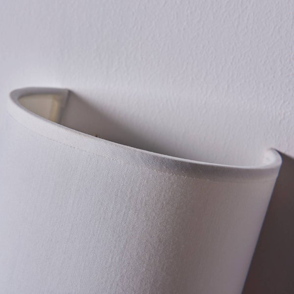 Detailansicht einer halbrunden Wandleuchte mit einem Lampenschirm aus Textilgewebe an einer strukturierten Wand.