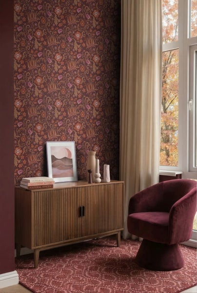Wohnraum mit floral gemusterter Tapete, einem Sideboard aus Holz, einem Polstersessel und einem gemusterten Teppich vor einem Fenster.