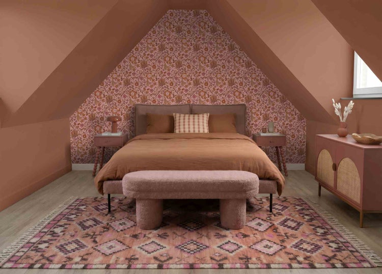 Gemütliches Schlafzimmer unter Dachschräge mit floraler Tapete, Doppelbett, Nachttischen, gemustertem Teppich, gepolsterter Bank und Holz-Sideboard.
