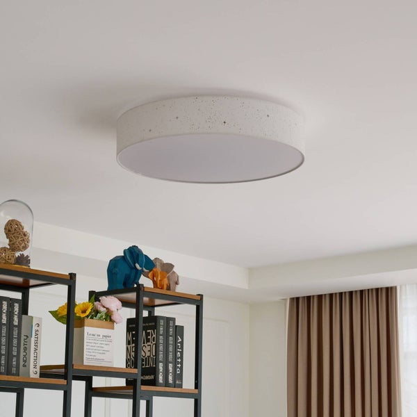 Runde Deckenleuchte mit Sternenmuster an der Seite, montiert an einer Decke in einem hellen Raum mit einem Regal darunter.