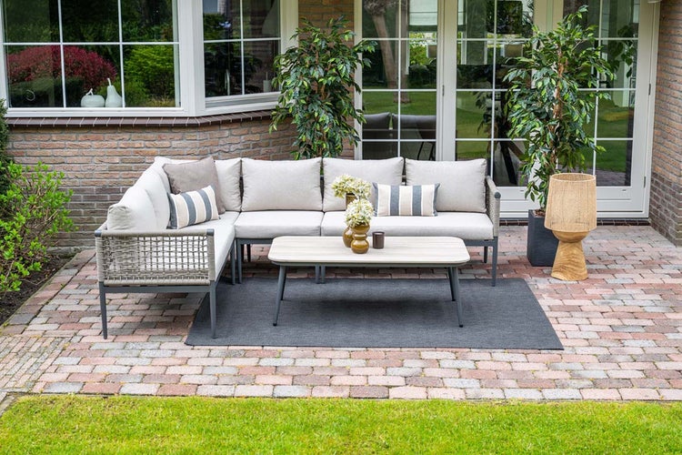 Modernes Garten-Lounge-Set auf gepflasterter Terrasse mit Ecksofa in Seiloptik, Couchtisch und Outdoorteppich.