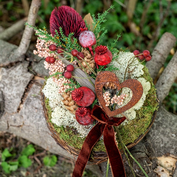 Gesteck mit Trockenblumen, Moos, Herz und Schleife in einem Korb