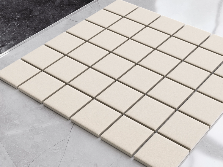 Quadratische Mosaikfliesen mit strukturierter Oberfläche auf einem marmorierten Boden in einer modernen Raumsituation.