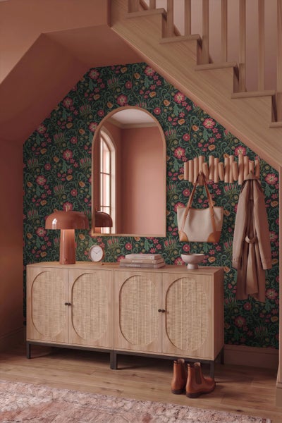 Hauseingang mit floraler Tapete, einem Bogen-Spiegel und einem Sideboard aus Holz mit Wiener Geflecht unter einer Treppe.