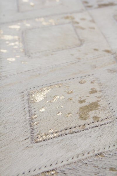 Nahaufnahme eines Kuhfell-Teppichs im Patchwork-Design mit goldfarbenen Akzenten und sichtbaren Nähten.
