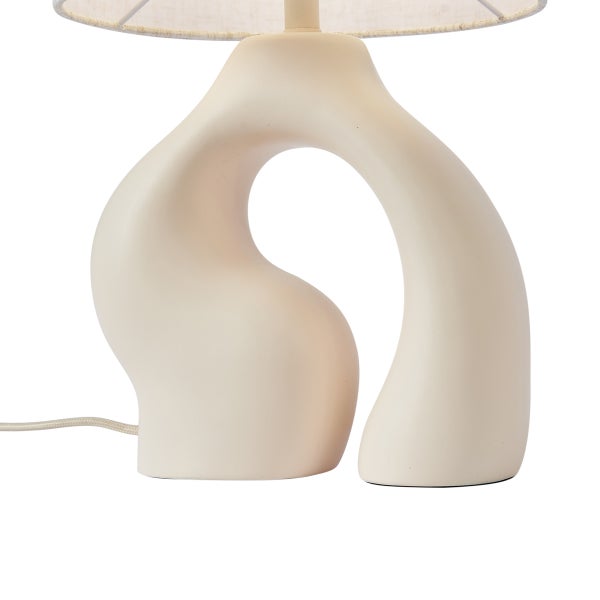 Organisch geformter Lampenfuß einer Tischleuchte aus Keramik mit textilem Lampenschirm.