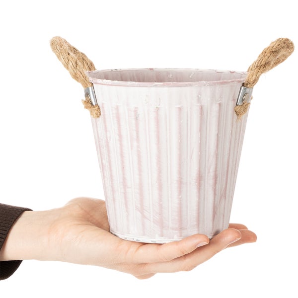 Kleiner rosa Metalleimer mit Seilgriffen und Rillenstruktur auf einer Hand präsentiert.