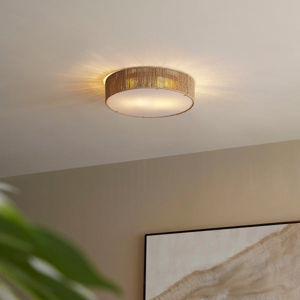 Runde Deckenleuchte im Boho-Stil mit einer Umrandung aus naturfarbenem Hanfseil und weißem Diffuser, eingeschaltet an einer Zimmerdecke.