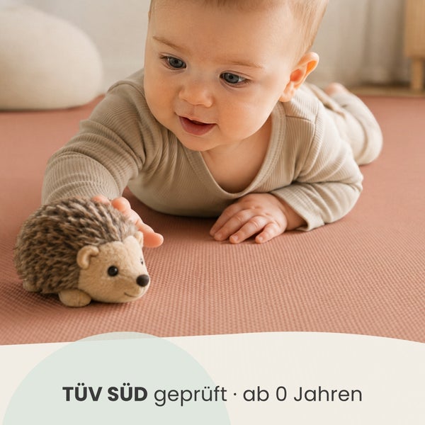 Ein Baby spielt auf einer Matte mit einem kleinen Stoffigel, der TÜV SÜD geprüft und für Kinder ab null Jahren geeignet ist.