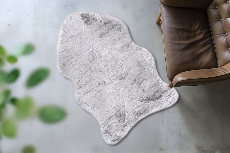 Flauschiger Kunstfell Teppich in Fellform liegend auf einem Boden neben einem Ledersessel.