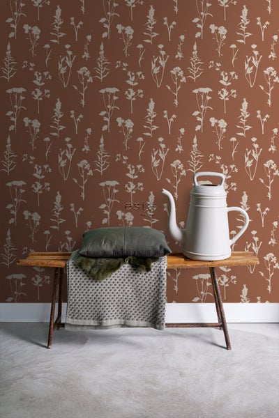 Dekoratives Stillleben mit einer Gießkanne und einer Bank vor einer floralen Tapete.
