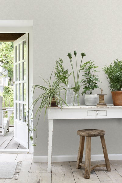 Dekorative Szene mit Tisch, Hocker und Pflanzen vor einer Tapete.