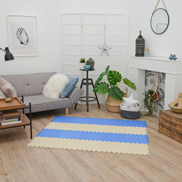 Ineinandergreifende Bodenschutzmatten aus Schaumstoff in Blau und Beige, gestreift ausgelegt in einem hellen Wohnzimmer mit grauem Sofa.