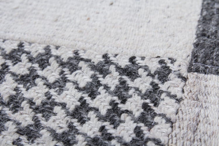 Nahaufnahme eines handgewebten Teppichs mit strukturiertem Webmuster in quadratischem Patchwork Design aus Wolle.